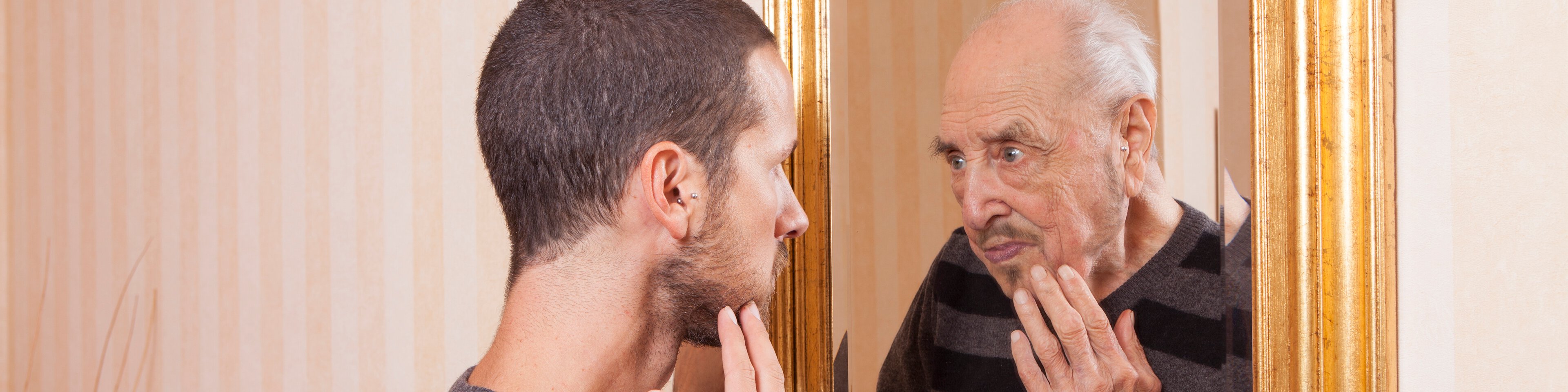 Ein junger Mann sieht in den Spiegel und sieht sich als alten Mann | © tommasolizzul - Getty Images/iStockphoto